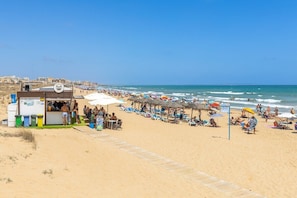A beach with a kiosk, umbrellas, and beach chairs.