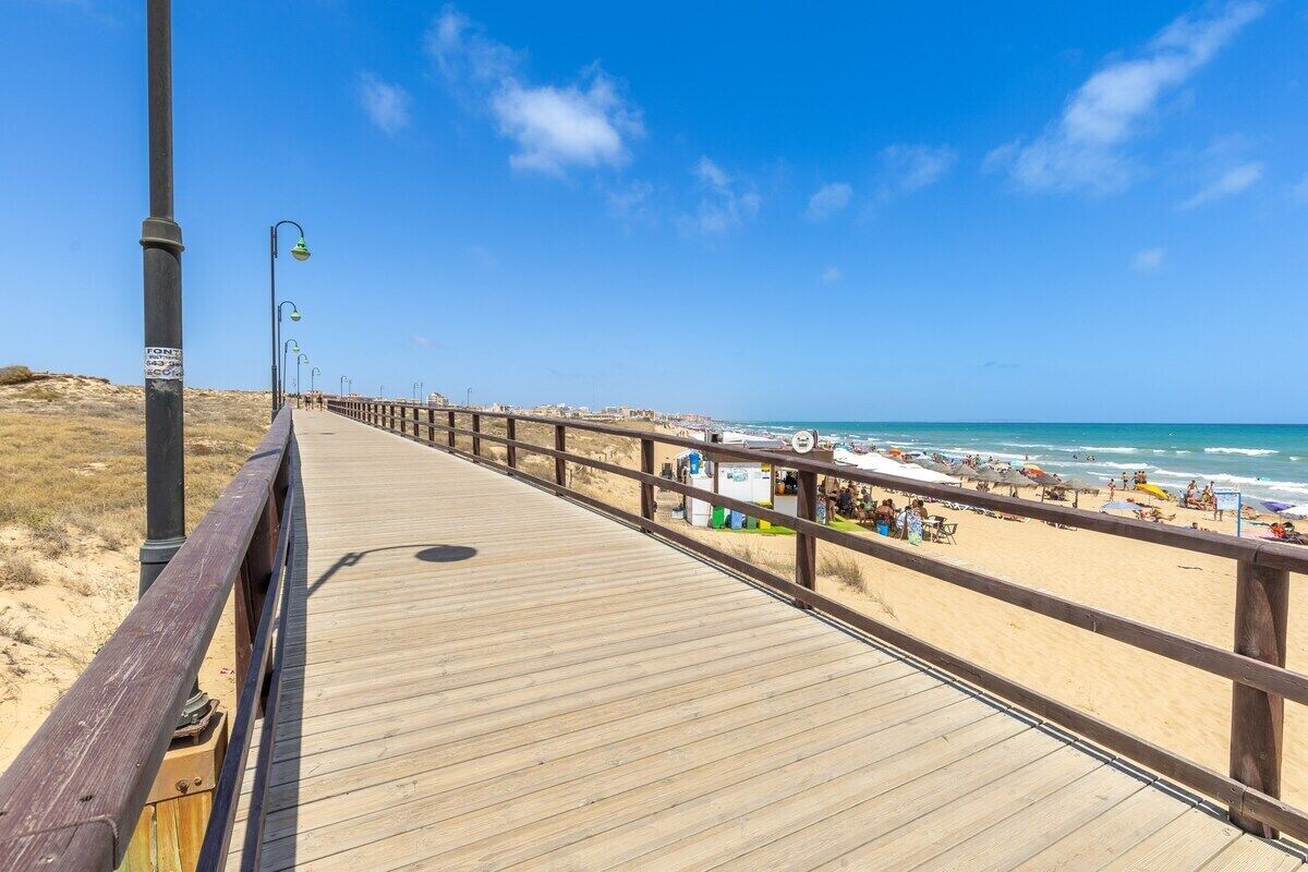 A wooden boardwalk leading to a beach with umbrellas and people.