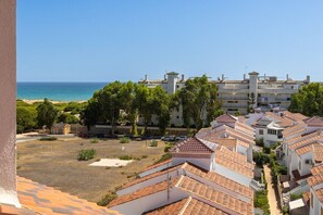A coastal residential area with terracotta-tiled buildings, a clear blue sky, and a beach in the background.