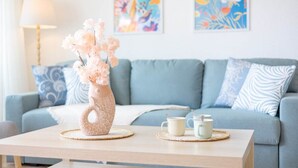 A living room with a light blue sofa, decorative pillows, a vase with flowers, and two cups on a wooden table.