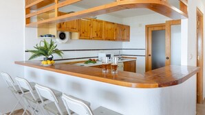 A kitchen with wooden cabinets, a white countertop, and a built-in bar area with bar stools.