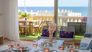 A dining area with a table set for four, a view of the sea, and a balcony with outdoor seating.