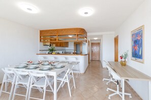 Une cuisine moderne avec un îlot central en bois, des chaises blanches et une table à manger dressée pour six personnes.