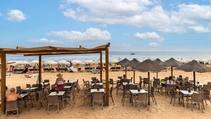 Ein Restaurant direkt am Strand mit Außenbereich, Sonnenschirmen und Blick auf den Strand und das Meer.