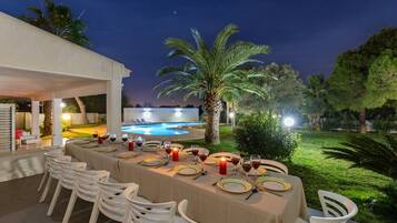 An outdoor dining area with a pool view, white chairs, and a table set for a meal.