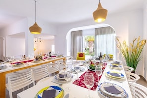 A dining area with white chairs, a long table set for a meal, and two hanging wicker lamps. - Fidalsa Luxurious Villa Salinas and Sea (Santa Pola)