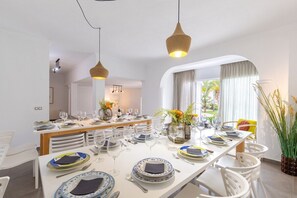 Een eethoek met een lange tafel gedekt voor een maaltijd, witte stoelen en hangende吊り下げ灯.