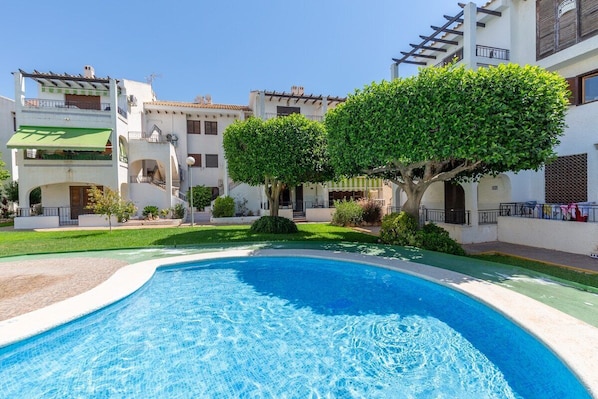 A swimming pool surrounded by white buildings with balconies and trees. - Flamingo Coast by Fidalsa (Orihuela)