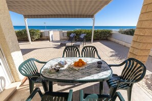 Un espace extérieur abrité, aménagé avec une table, des chaises et offrant une vue sur la mer.