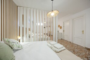 A hotel room with a bed, a bedside lamp, a mirror, a door, and a wall with vertical blinds. - Fidalsa Grand White House (Mutxamel)