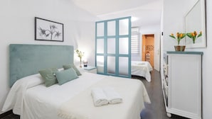 A hotel room with a bed, a nightstand, a dresser, and a bathroom visible through a frosted glass door.