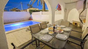 A dining area with a pool view, outdoor seating, and a spiral staircase.