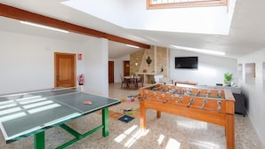 Ein Raum mit Tischtennisplatte, Kicker, Kamin, Fernseher und einem Fenster.