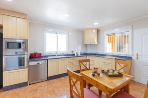 A modern kitchen with wooden cabinets, a built-in oven, microwave, and dishwasher. There is a dining table with chairs and a window with curtains. - Fidalsa Dom Perignon (Crevillente)