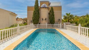A swimming pool with a white fence and a building with a dome and two tall trees in the background. - Fidalsa Mediterranean Beachfront (Orihuela)
