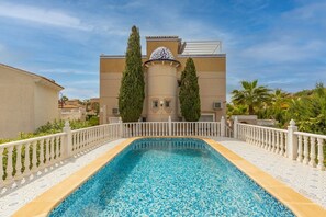 A swimming pool with a white fence and a building with a dome and two tall trees in the background. - Fidalsa Mediterranean Beachfront (Orihuela)