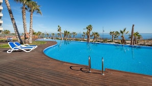 A clear blue pool with wooden deck and lounge chairs, surrounded by palm trees and a view of the sea. - Fidalsa Paradise Sea Punta Prima (Torrevieja)