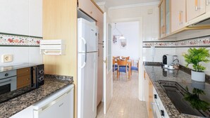 A compact kitchen with a refrigerator, stove, and dining area. - Beach Haven by Fidalsa (Guardamar del Segura)