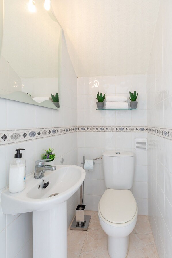 A bathroom with a white sink, a toilet, and a mirror. There are two potted plants on a shelf above the toilet. - Goldencore by Fidalsa (Orihuela)