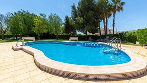 A swimming pool with a tiled edge, surrounded by a patio area with a bench and a palm tree. - Goldencore by Fidalsa (Orihuela)
