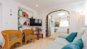 A living room with wicker chairs, a sofa, a flat-screen TV, and a kitchen in the background. - Fidalsa Coastal Soul (Torrevieja)