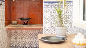 Una cocina con salpicadero de azulejos, una lámpara colgante, una planta en maceta y un frutero sobre la encimera.