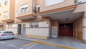 Un edificio con entrada protegida por una reja, un coche estacionado y suelo de baldosas.