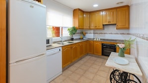 Una cocina con armarios de madera, un refrigerador blanco, lavavajillas, un lavamanos y una pequeña mesa con un florero.