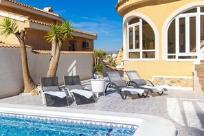 A poolside area with lounge chairs and a small table, surrounded by palm trees and a building with arched windows. - The Big Chill by Fidalsa (Rojales)