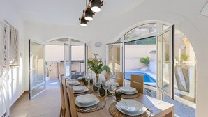 A dining area with a long table set for six, large windows, and a view of a swimming pool. - The Big Chill by Fidalsa (Rojales)