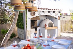Un área de comedor al aire libre con pared de piedra, horno de pizza y mesa dispuesta para una comida.