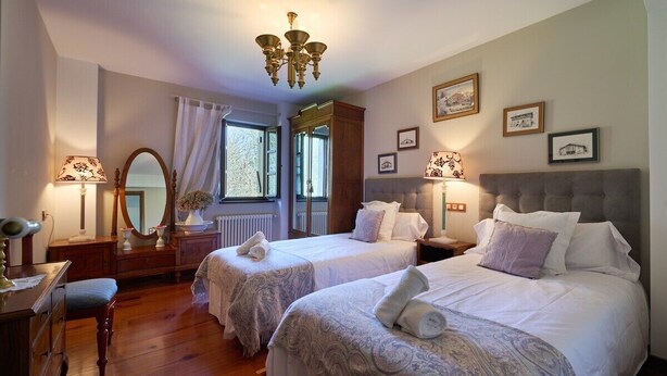 A hotel room with two beds, a mirror, a dresser, a chair, and a chandelier. - The Basque Experience by Fidalsa (Otxandio)
