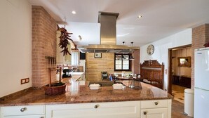 A kitchen with a granite countertop, white cabinetry, a hanging pot rack, and a stainless steel range hood. - The Basque Experience by Fidalsa (Otxandio)