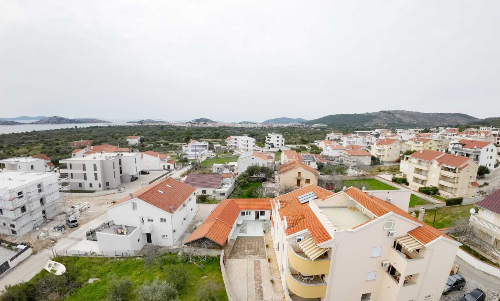 A residential area with apartment buildings, some with balconies, and a hilly landscape in the background.