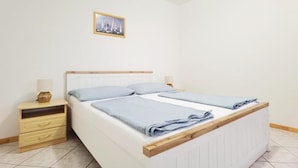Ein Einzelbett mit Holz-Kopfteil, ein Nachttisch mit Lampe und ein gerahmtes Bild an der Wand.