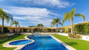 A swimming pool with a curved design, surrounded by well-maintained grass and palm trees. - Happiness Corner by Fidalsa (Pilar de la Horadada)