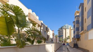Una strada residenziale con edifici moderni, un percorso pedonale lastricato e palme.