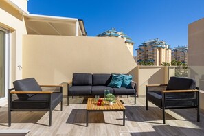 Ein Balkon mit einer Couch, zwei Sesseln und einem Couchtisch mit Früchten und einer Pflanze.