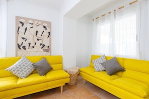 A bright yellow sofa with patterned cushions, a woven basket, and a large abstract painting on the wall. - Fidalsa Divine Hiding (Algorfa)