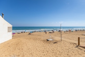 A beach with a white building, umbrellas, and people. - Laguna Dream by Fidalsa (Guardamar del Segura)