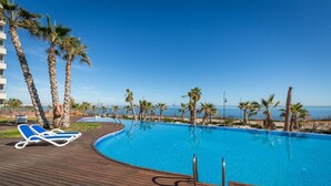 Ein Swimmingpool mit Holzterrasse, Palmen und freiem Blick auf den Ozean.