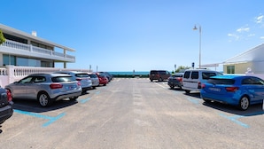 A parking lot with multiple cars, a building with a balcony, and a clear view of the sea in the background. - Ocean Blue Eyes by Fidalsa (Guardamar del Segura)