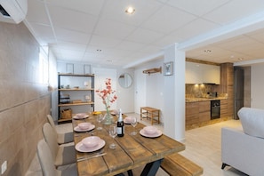 Comedor con una mesa de madera dispuesta para cuatro, cocina con electrodomésticos modernos y una paleta de colores neutros.