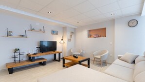 A modern living room with a flat-screen TV, wooden coffee table, sofa, and a wall-mounted clock. - Ocean Blue Eyes by Fidalsa (Guardamar del Segura)