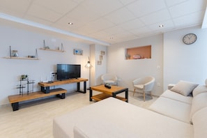 A modern living room with a flat-screen TV, wooden coffee table, sofa, and a wall-mounted clock.