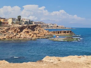 A coastal area with rocky terrain and buildings in the background. - Fidalsa Moon Dunes Villa (Torrevieja)