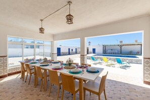 Ein Essbereich mit einem Tisch für sechs Personen, großen Fenstern und Blick auf einen Pool sowie Gebäude.
