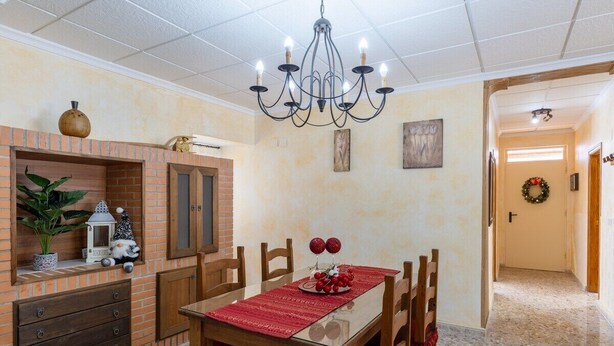 Un coin repas agrémenté d’une cheminée en briques, d’une table en bois, de chaises et d’un lustre.