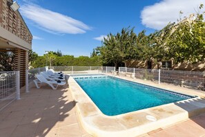 Ein rechteckiger Pool mit einer Fliesenbordur, umgeben von einem weißen Zaun, neben einem Gebäude mit Ziegelaußenwand.