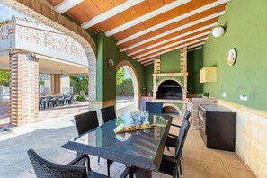 Eine Außenpatio mit einem Glastisch, Korbstühlen, einem Kamin aus Backsteinen und einer grünen Wand.